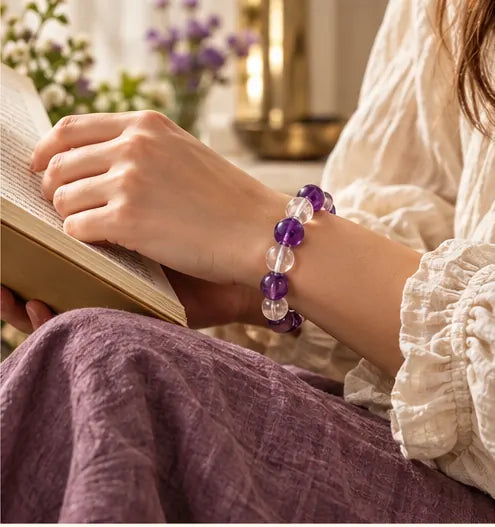 Woman wearing amethyst and clear crystal bracelet while reading beside a window