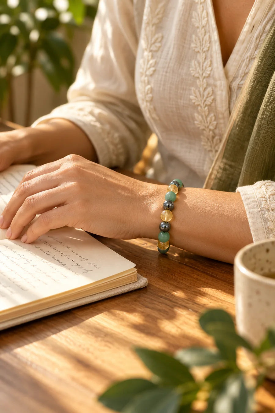 Woman wearing a grey, yellow and green bracelet while writing at a sunlit desk