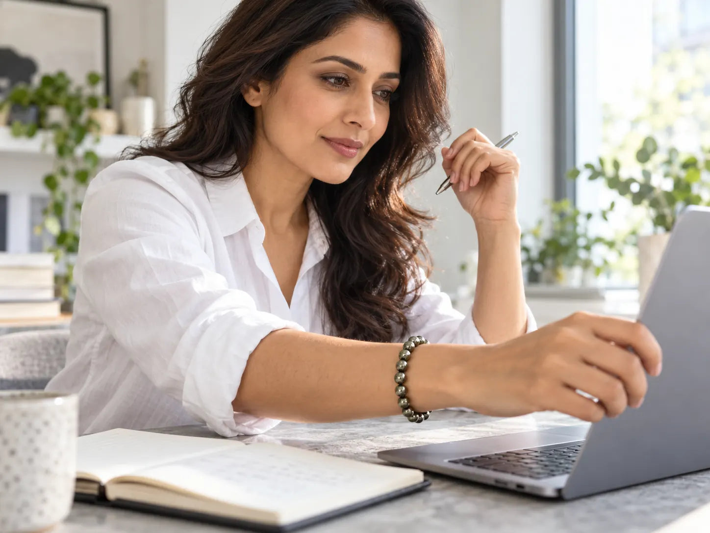 An Indian woman begins work at her laptop, wearing a metallic-grey bead bracelet