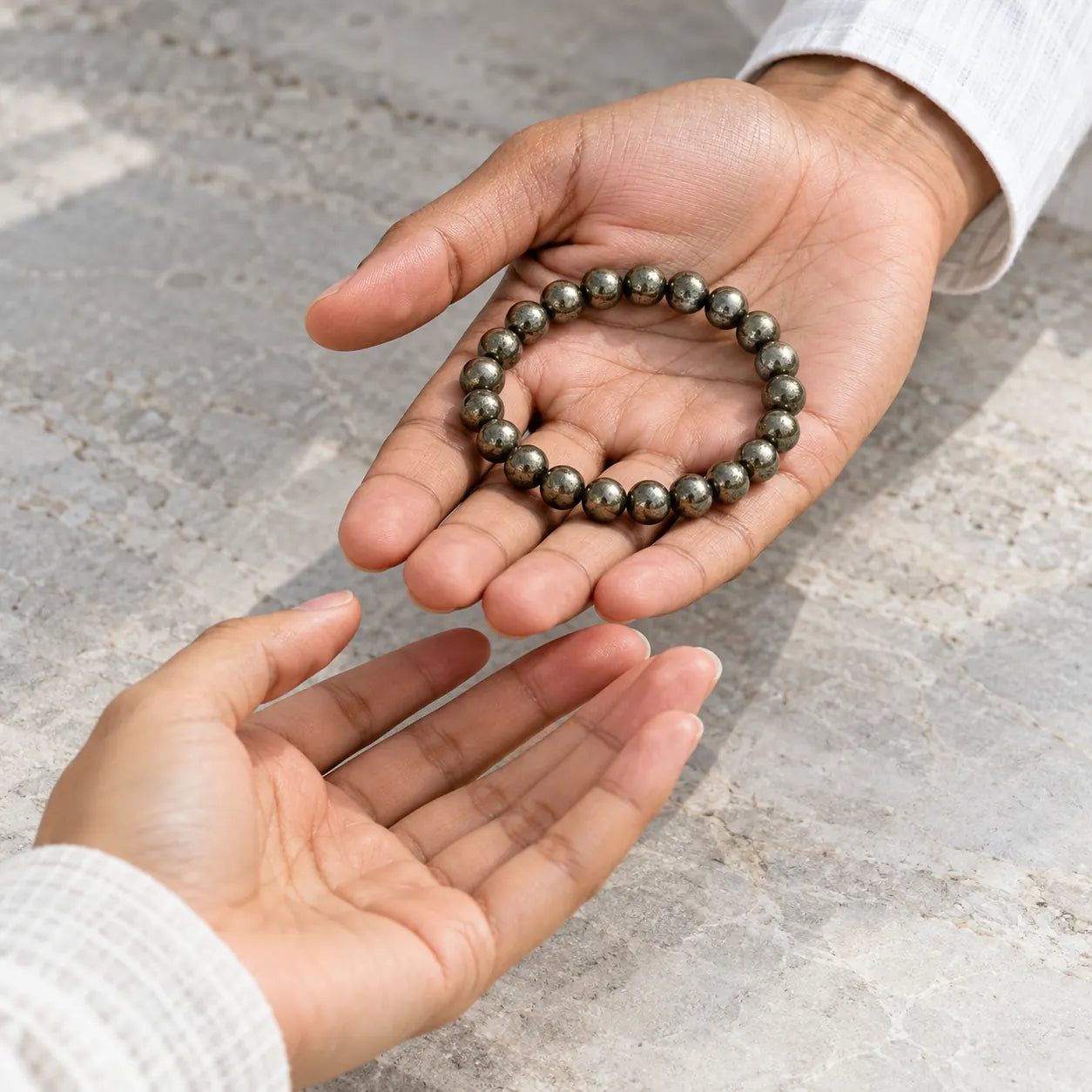 A metallic Pyrite bead bracelet offered from one person’s open palm to another
