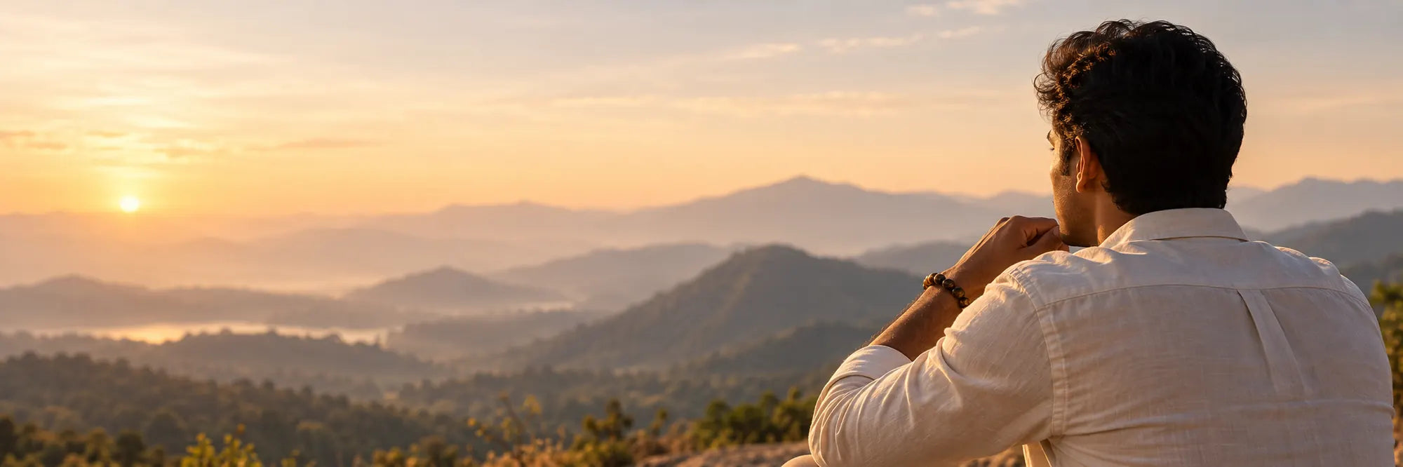 Person wearing a Tiger Eye bracelet pauses while looking across warm hills at dawn