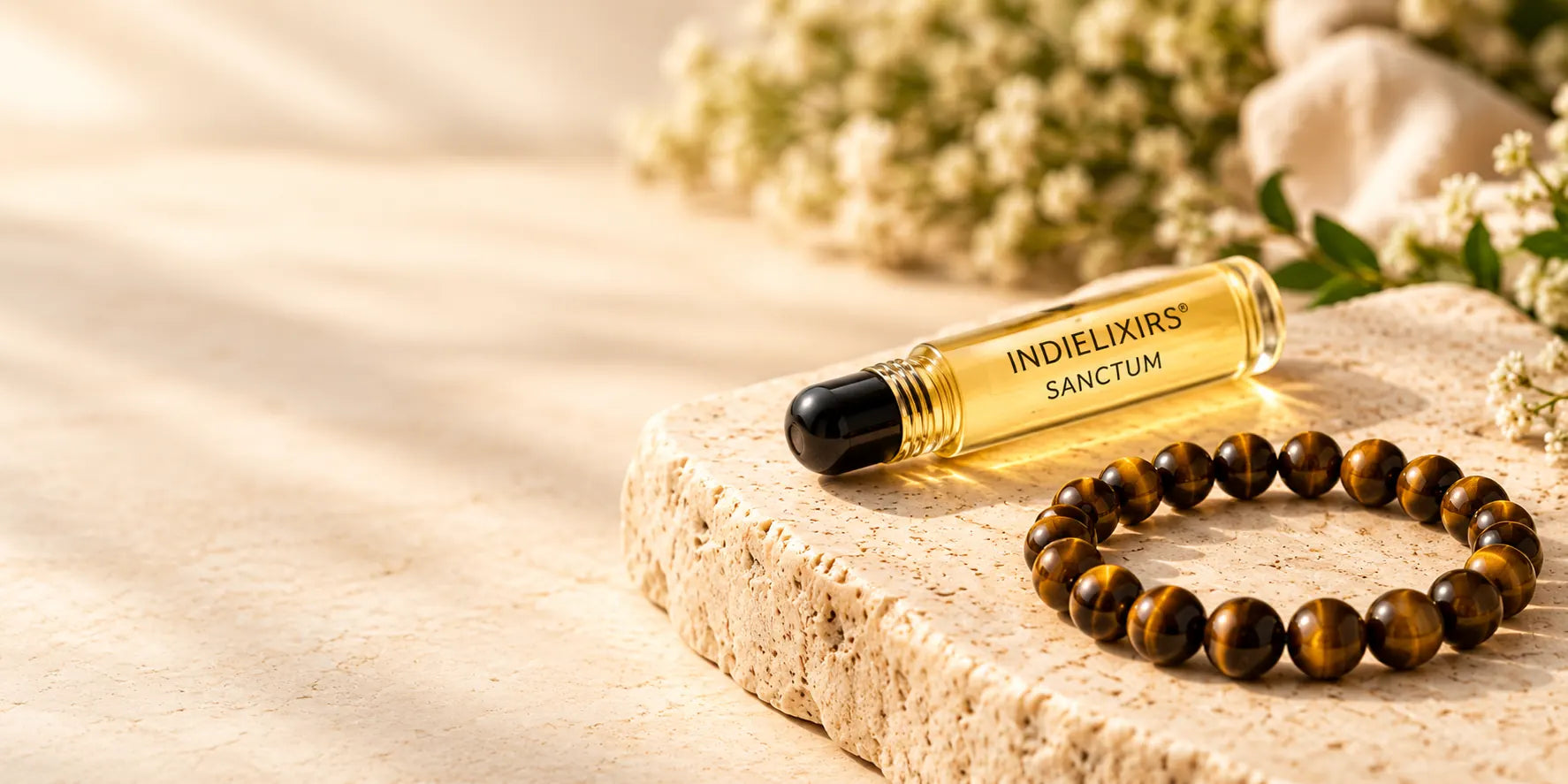 INDIELIXIRS SANCTUM aromatic roller beside a dry Tiger Eye bracelet on warm ivory stone